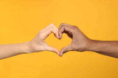 Photo of International relationships. People making heart with hands on orange background, closeup