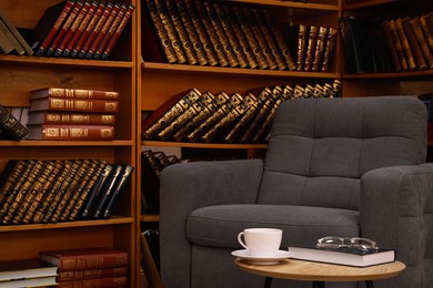 Book with glasses and cup of drink near comfortable armchair in cozy home library