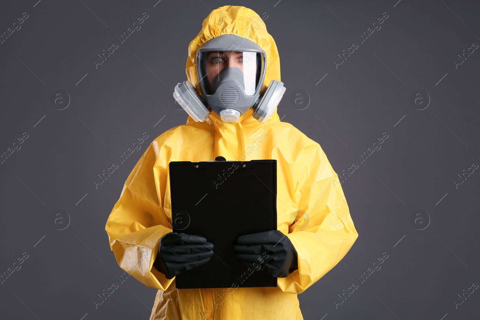 Photo of Woman in chemical protective suit holding clipboard on grey background. Virus research