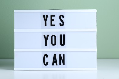 Photo of Lightbox with phrase Yes You Can on table against light green background. Motivational quote