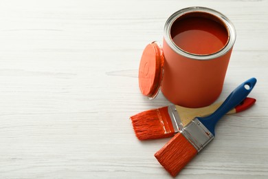 Photo of Can of orange paint and brushes on white wooden table. Space for text