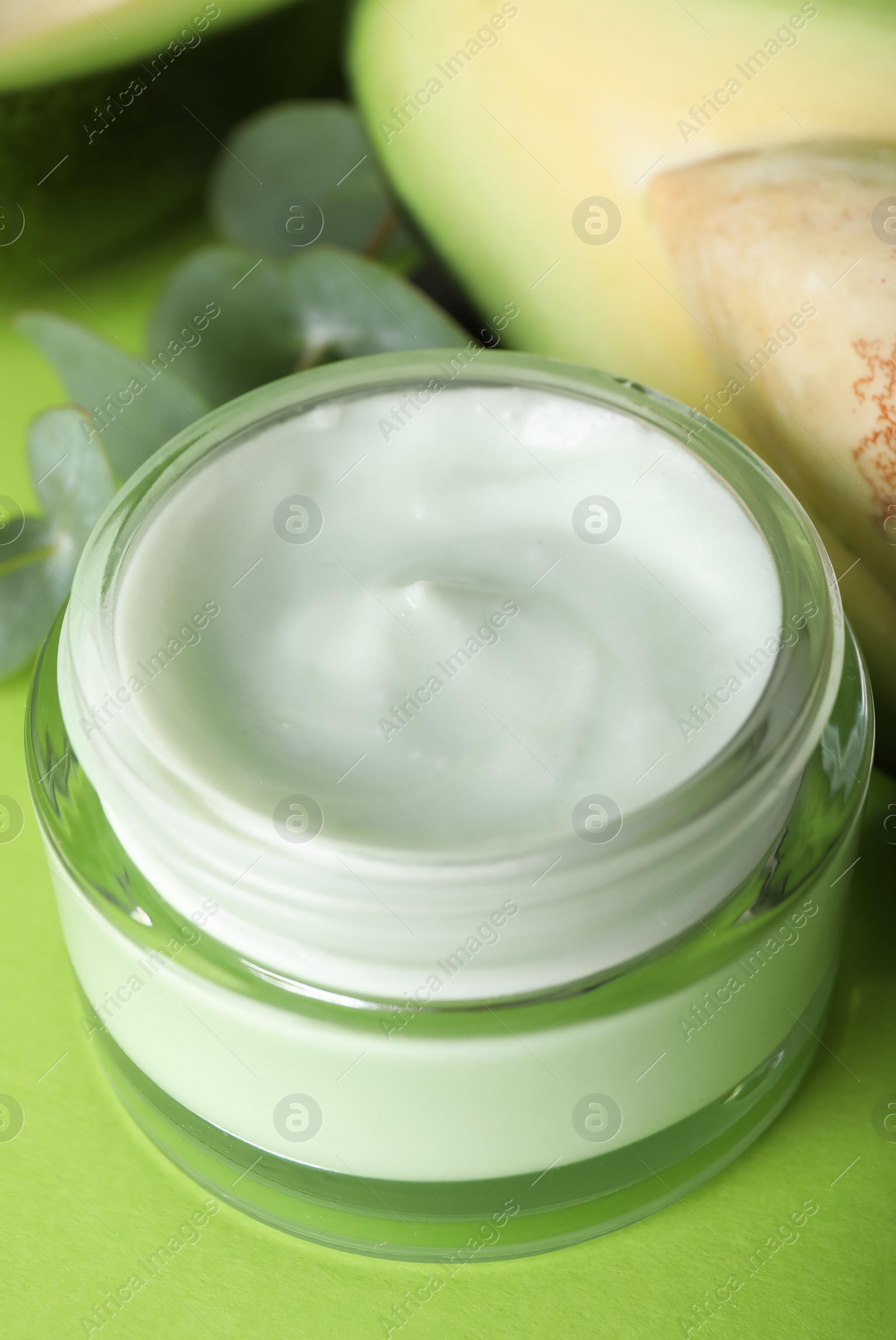 Photo of Jar of body cream with eucalyptus and avocado on light green background, closeup