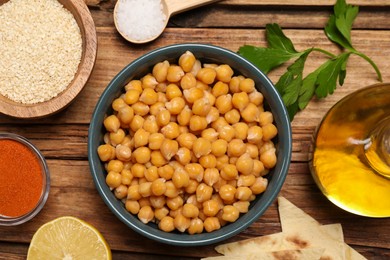 Photo of Delicious chickpeas and different ingredients on wooden table, flat lay. Cooking hummus