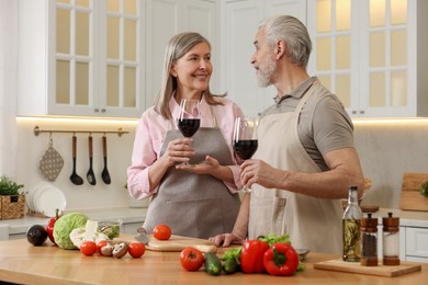 Happy senior couple with glasses of wine cooking together in kitchen