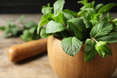 Wooden mortar with fresh green mint on table, closeup. Space for text