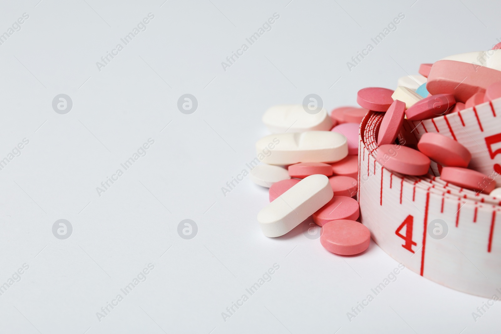 Photo of Weight loss pills and measuring tape on white background. Space for text