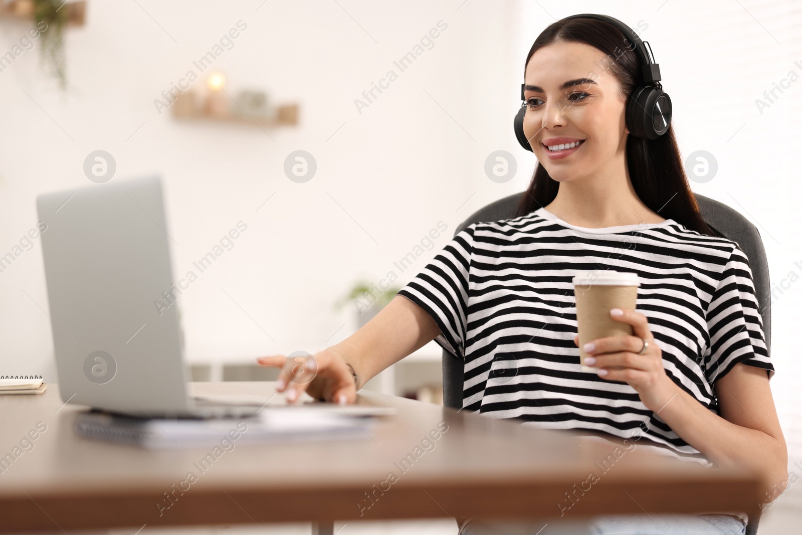 Photo of Young woman in headphones watching webinar at table in room