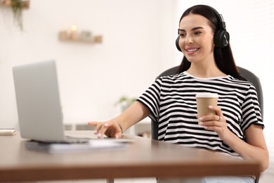 Young woman in headphones watching webinar at table in room