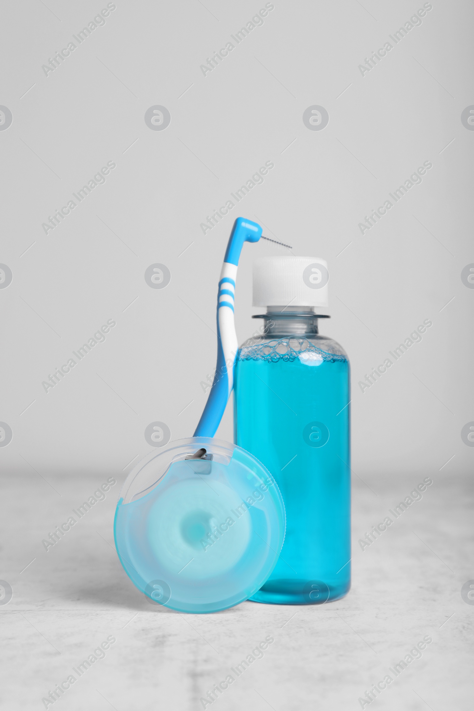 Photo of Dental floss and different teeth care products on light grey textured table