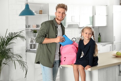 Happy father putting textbooks into little child's school bag in kitchen
