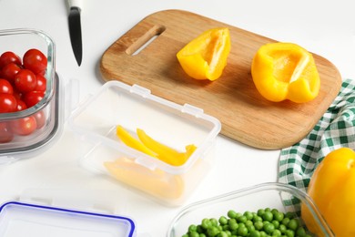 Photo of Wooden board with cut bell pepper and containers with fresh products on white table. Food storage