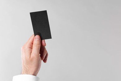 Man holding blank business card on light grey background, closeup. Space for text