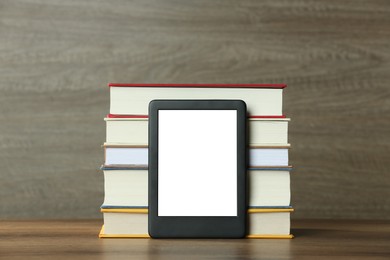 Photo of Portable e-book reader and stack of hardcover books on wooden table