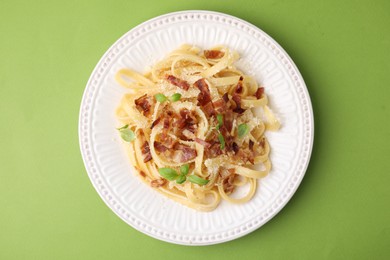 Photo of Tasty pasta with bacon and basil on light green table, top view