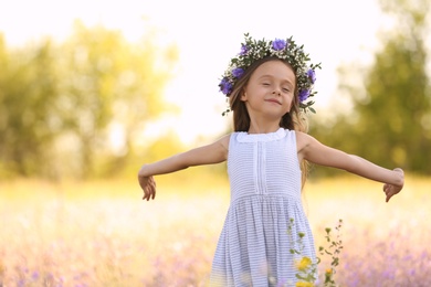 Photo of Cute little girl wearing flower wreath outdoors. Child spending time in nature