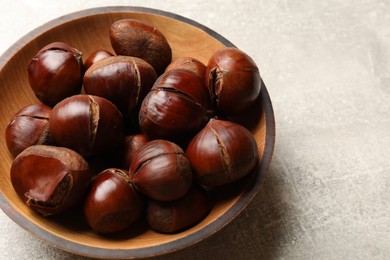Photo of Fresh edible sweet chestnuts in wooden bowl on grey table, closeup