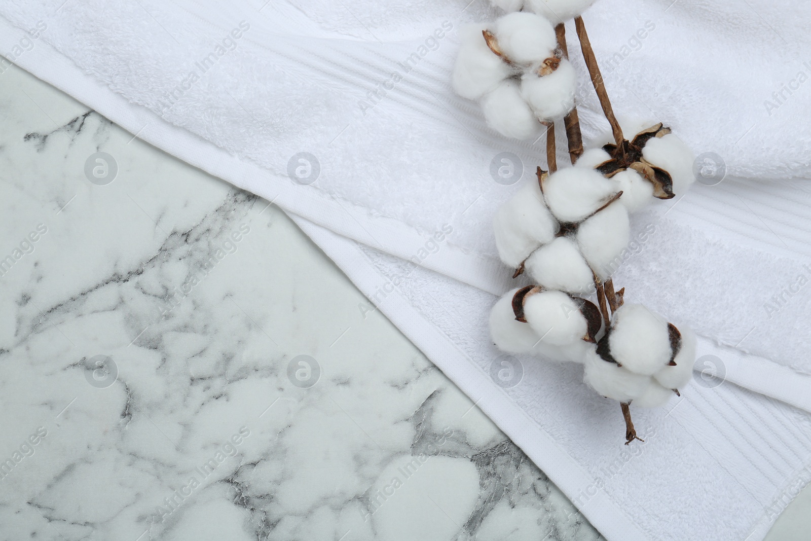 Photo of Terry towel and cotton flowers on white marble table, top view. Space for text