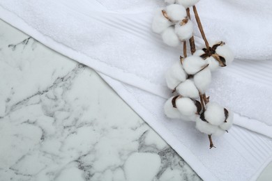 Terry towel and cotton flowers on white marble table, top view. Space for text