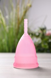 Pink menstrual cup on light table indoors, closeup