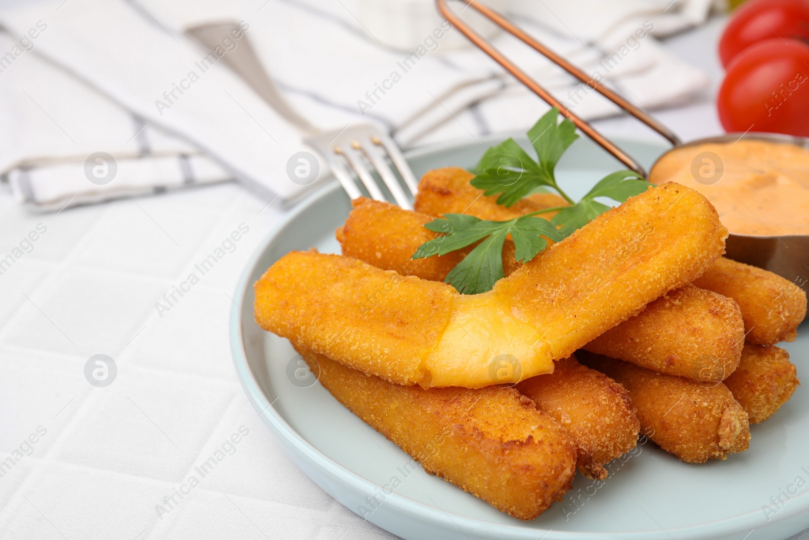 Photo of Tasty fried mozzarella sticks served with sauce and parsley on white tiled table, space for text
