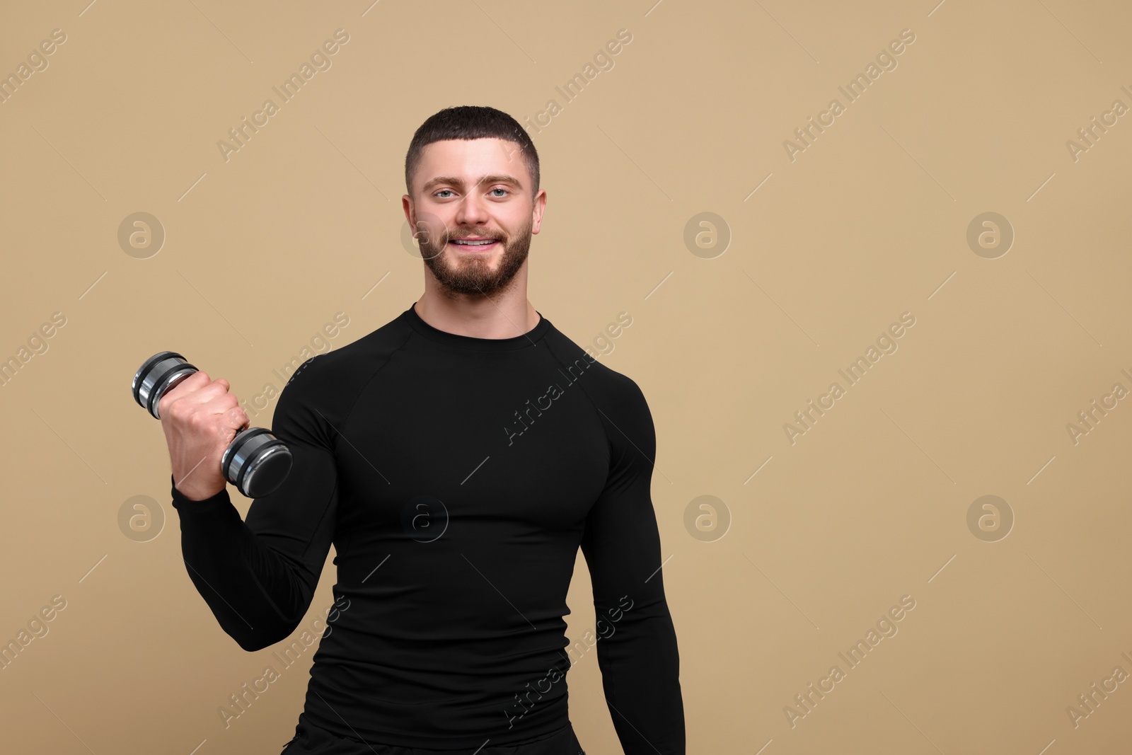 Photo of Handsome sportsman exercising with dumbbell on brown background, space for text