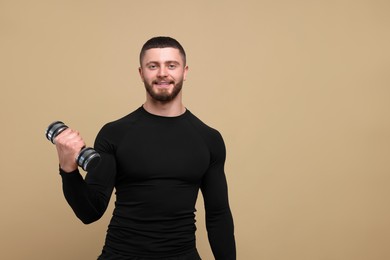 Handsome sportsman exercising with dumbbell on brown background, space for text