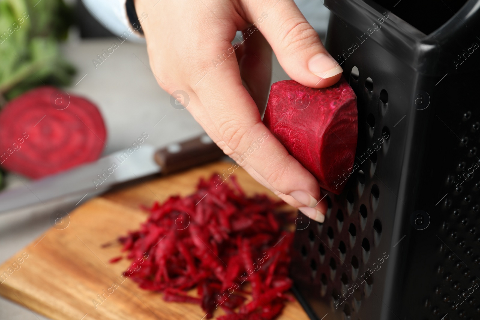 Photo of Woman grating fresh red beet at table, closeup