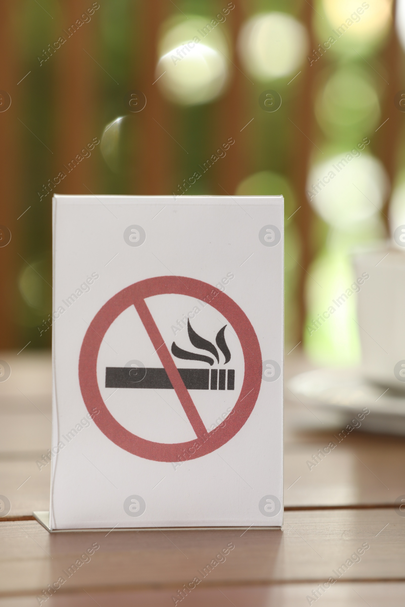 Photo of No Smoking sign on wooden table against blurred background, closeup
