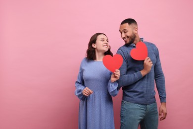 Photo of Lovely couple with red paper hearts on pink background, space for text. Valentine's day celebration
