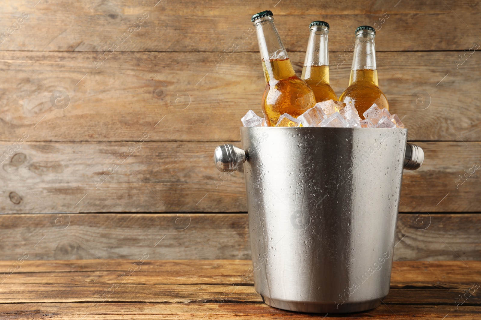 Photo of Metal bucket with beer and ice cubes on wooden background. Space for text