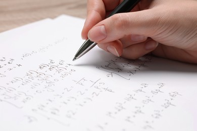 Student writing different mathematical formulas on paper, closeup