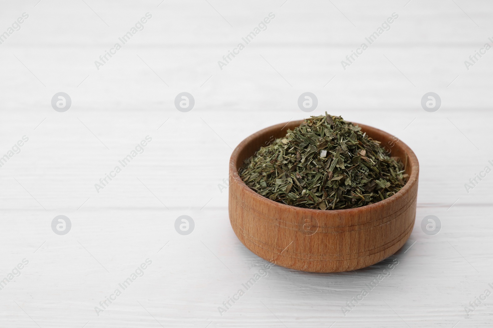 Photo of Bowl of dry tarragon on white wooden table. Space for text