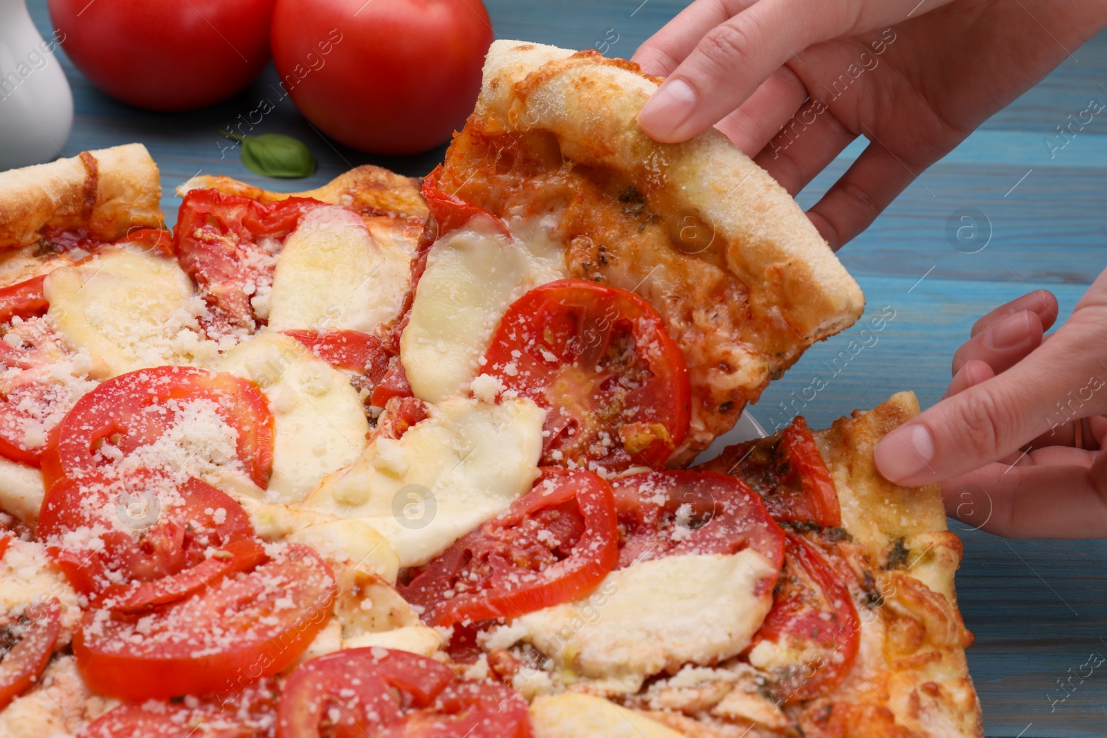 Photo of Woman taking piece of delicious Caprese pizza at blue wooden table, closeup