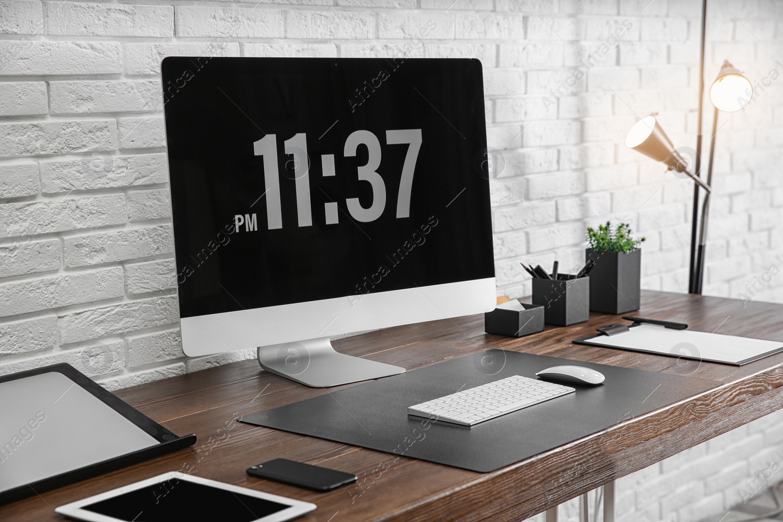 Photo of Modern workplace interior with computer and devices on table near brick wall