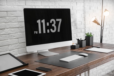 Modern workplace interior with computer and devices on table near brick wall