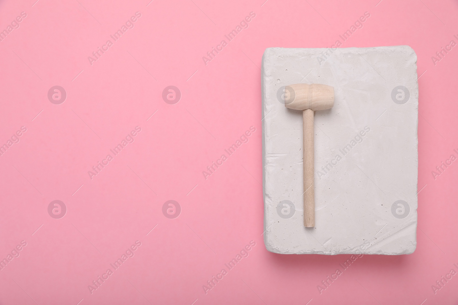 Photo of Educational toy for motor skills development. Excavation kit (plaster and wooden mallet) on pink background, top view with space for text