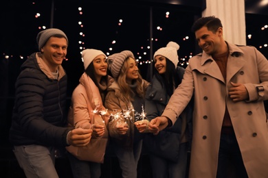 Photo of Group of people holding burning sparklers at night, focus on hands