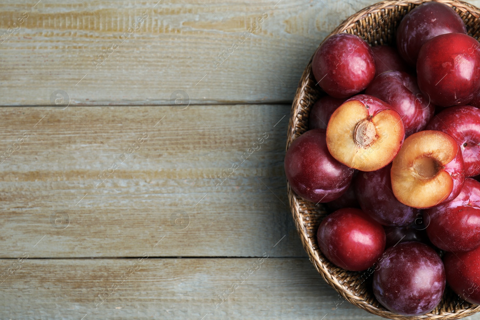 Photo of Delicious ripe plums in wicker bowl on wooden table, top view. Space for text