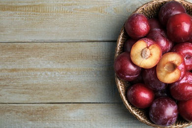 Photo of Delicious ripe plums in wicker bowl on wooden table, top view. Space for text