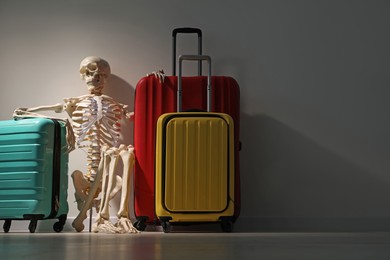 Waiting concept. Human skeleton with suitcases near grey wall, space for text