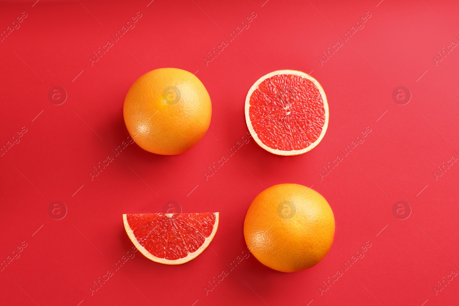 Photo of Cut and whole ripe grapefruits on red background, flat lay