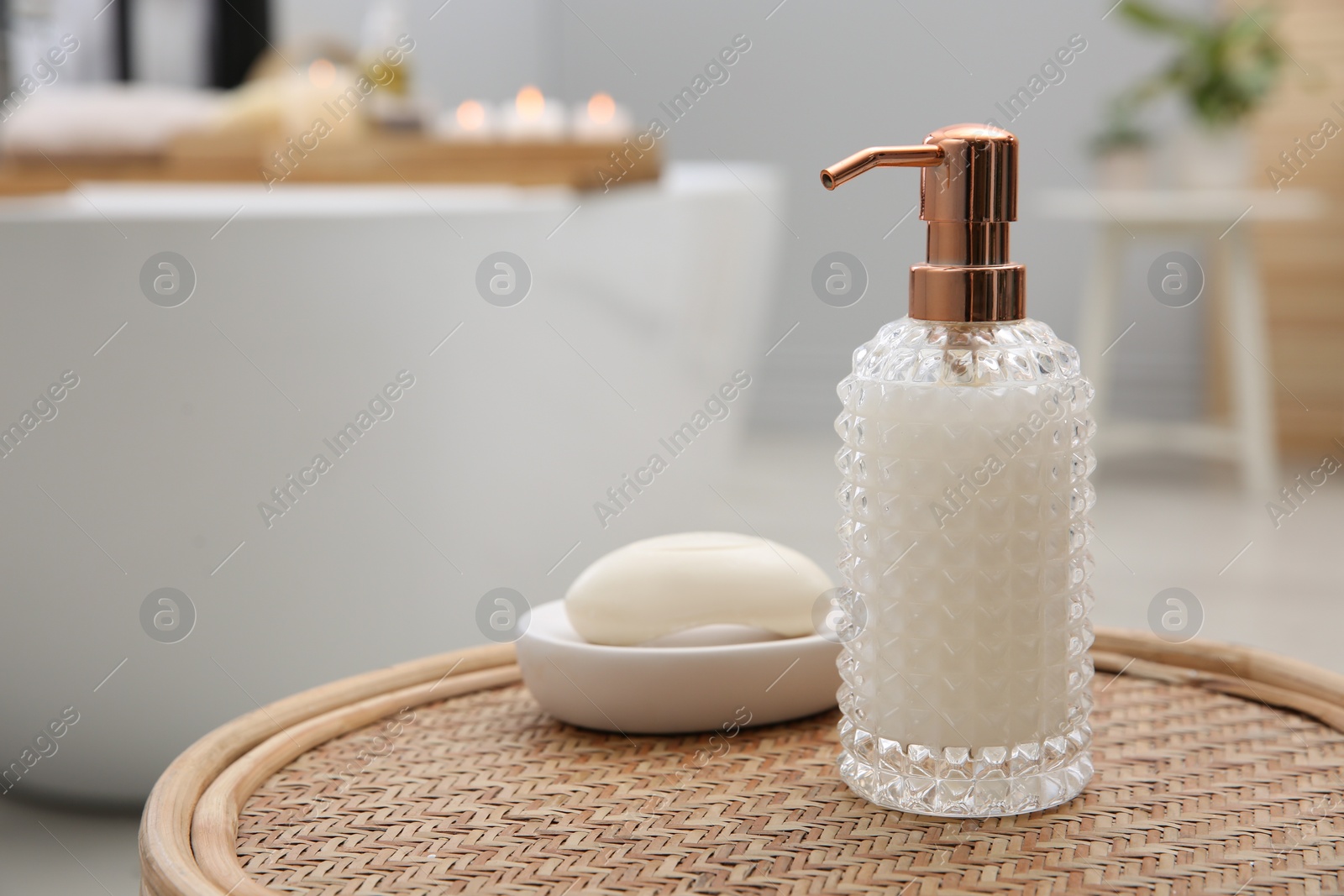 Photo of Stylish glass dispenser and soap bar on wicker stool in bathroom. Space for text
