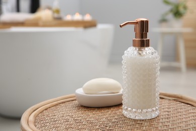 Photo of Stylish glass dispenser and soap bar on wicker stool in bathroom. Space for text