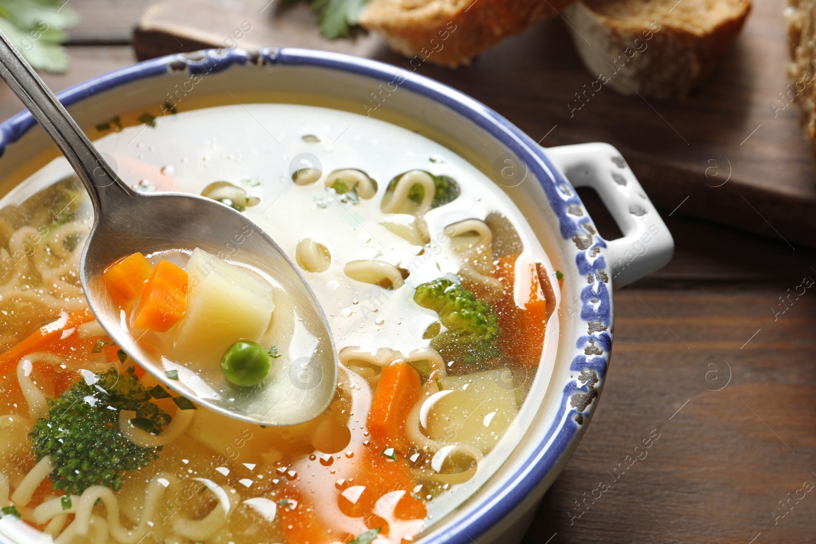 Photo of Spoon of fresh homemade vegetable soup over full dish on wooden table, closeup