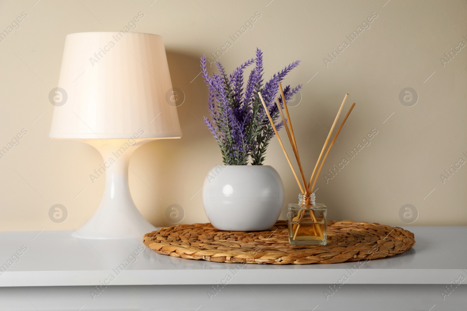 Photo of Aromatic reed air freshener, lamp and lavender flowers on white table indoors