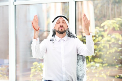 Photo of Muslim man with misbaha praying near windows indoors