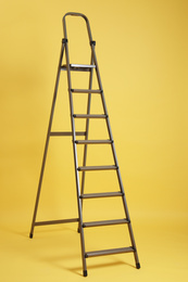 Photo of Modern metal stepladder on yellow background. Construction tool