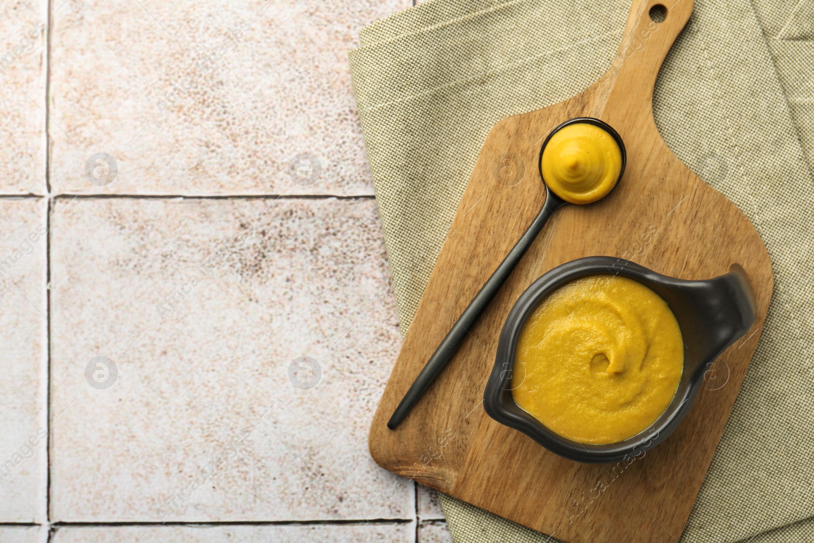 Photo of Tasty mustard sauce on light tiled table, top view. Space for text