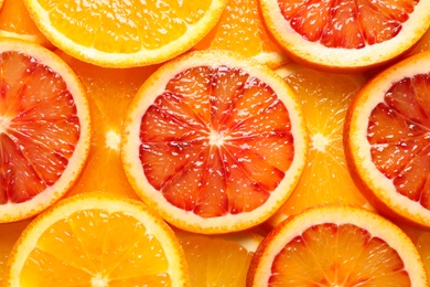 Photo of Slices of fresh citrus fruits as background, top view