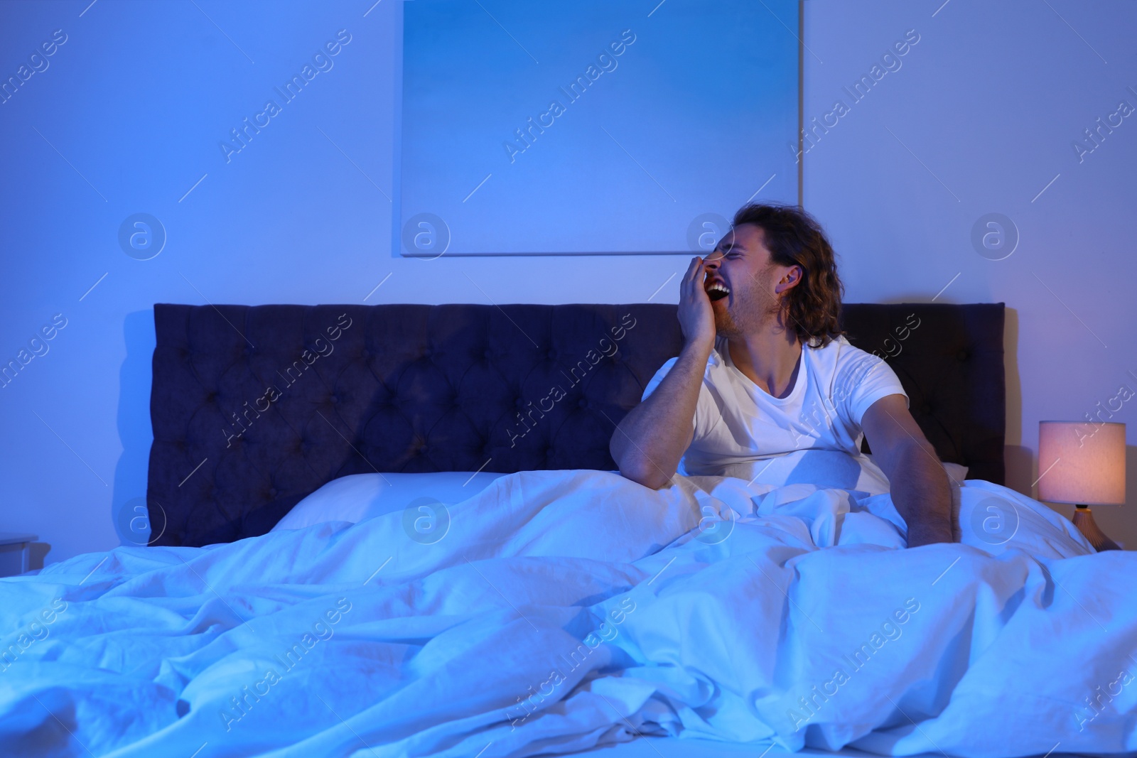 Photo of Sleepy young man yawning in dark room at night. Bedtime